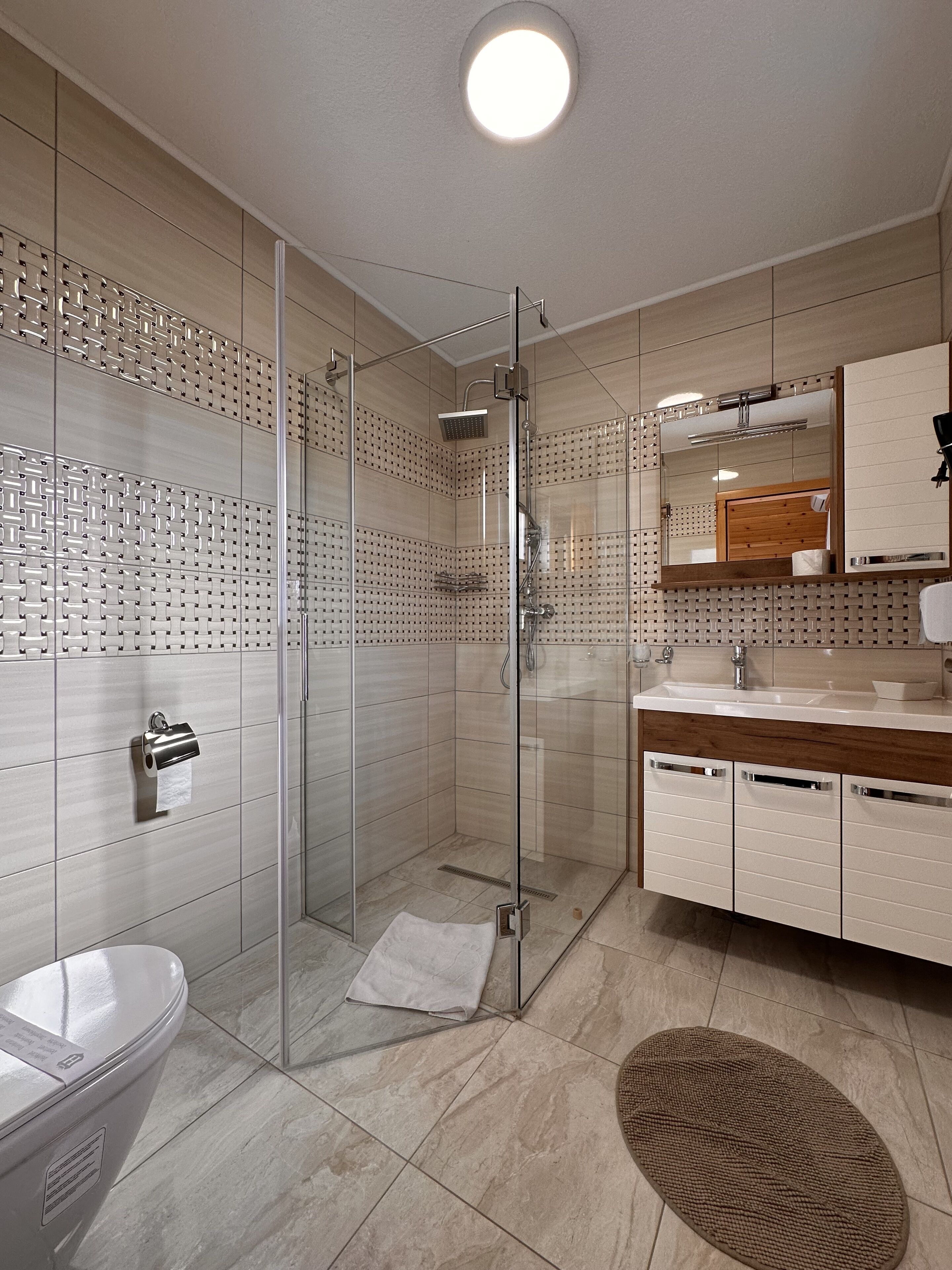 A modern bathroom with a glass-enclosed shower, a toilet, a sink with a wooden vanity, and a mirror.