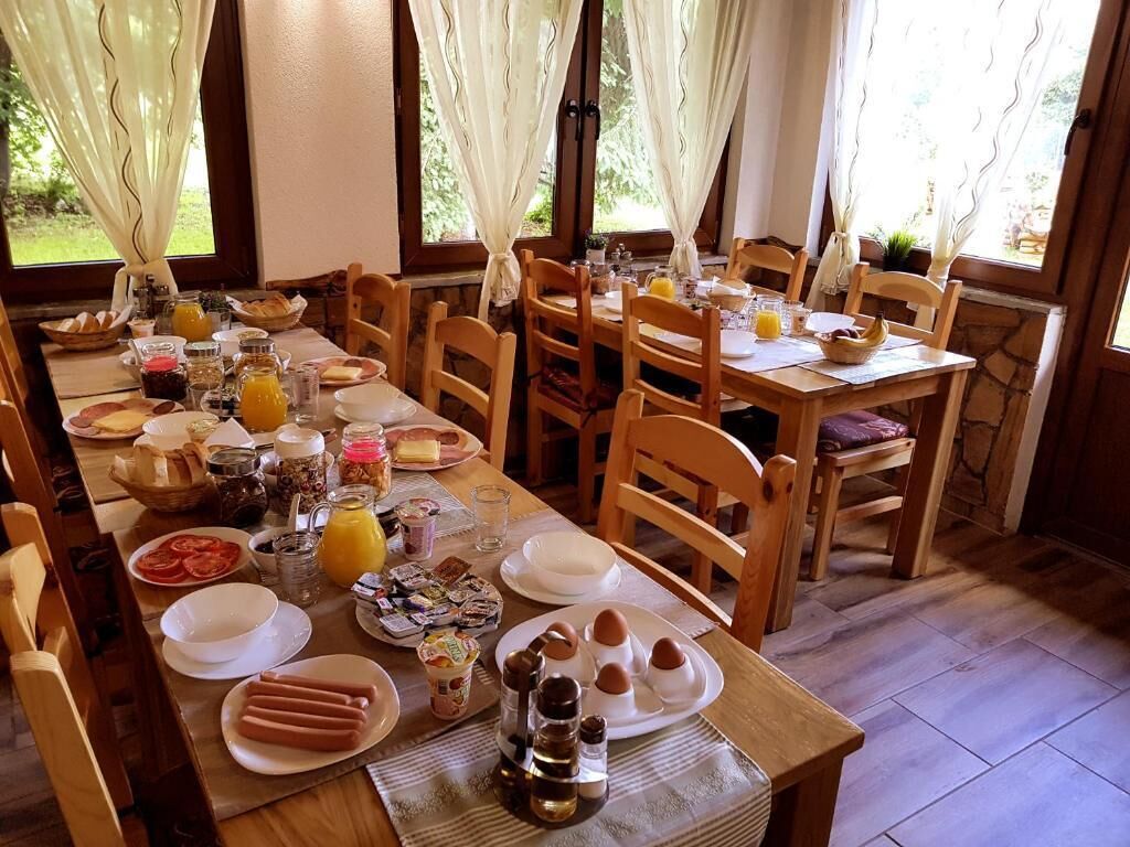 A breakfast setting with a long wooden table, chairs, and various breakfast items like eggs, bread, and fruit.