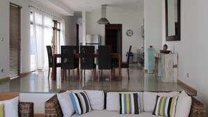 A spacious living area with a sofa, chairs, a dining table, and a kitchen in the background.