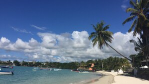 A beach with boats, palm trees, and a temple-like structure.