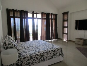 Un dormitorio con cama, cortinas, televisor y una mesita.