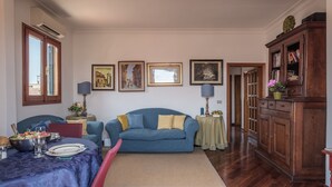 A living room with a blue sofa, a dining table set with plates and a bowl of fruit, and a wooden cabinet. - Florence Duomo View (Florence)