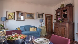 A dining area with a table set for two, a blue sofa, and a wooden cabinet with books. - Florence Duomo View (Florence)