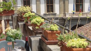 A terrace with a table set for two, surrounded by potted plants and a view of a building with classical architecture. - Florence Duomo View (Florence)