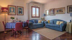 A living room with a dining area, featuring a blue sofa, a red chair, a dining table set with plates and glasses, and framed artwork on the walls. - Florence Duomo View (Florence)