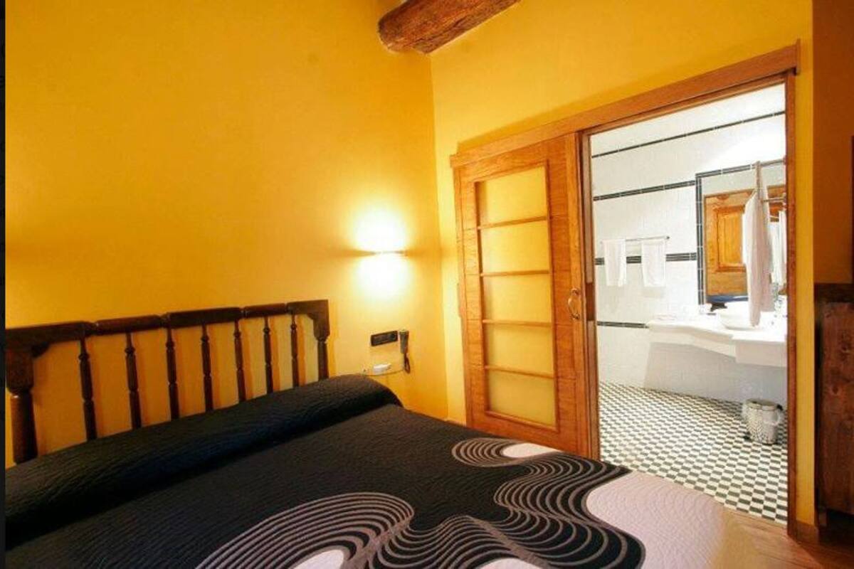 Ein Schlafzimmer mit einem Bett, einem Nachttisch, einer Wandlampe und einem durch eine offene Tür einsehbaren Badezimmer.