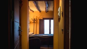 A narrow hallway leading to a bedroom with a bed, a coat rack, and a window with curtains. - A Corona del Reino (Ejea De Los Caballeros)