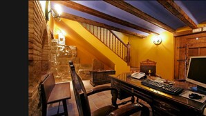 A rustic room with a wooden desk, a computer, a telephone, and a stone wall. - A Corona del Reino (Ejea De Los Caballeros)