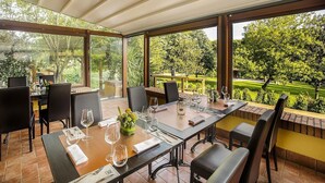 Un coin repas avec une table dressée pour quatre personnes, entourée de chaises, et de grandes fenêtres donnant sur un jardin magnifiquement entretenu.