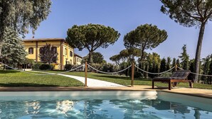 Une piscine offrant une vue dégagée sur un bâtiment situé à l’arrière-plan, entourée d’arbres et délimitée par une barrière faite de cordes.