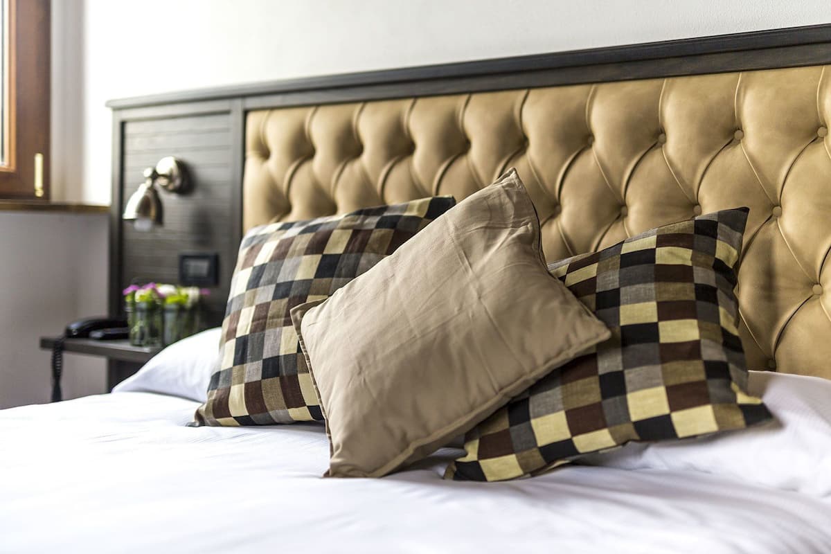 A bed with a tufted headboard, two pillows, and a nightstand with a lamp and decorative items.