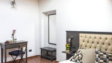 A hotel room with a bed, a desk, a chair, a small table, a mirror, and a nightstand.
