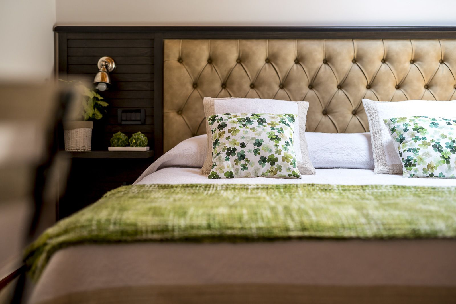 A neatly made bed with a tufted headboard, two floral-patterned pillows, and a green throw blanket.