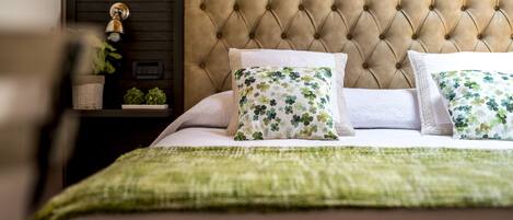 A neatly made bed with a tufted headboard, two floral-patterned pillows, and a green throw blanket.