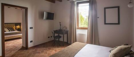 A bedroom with a bed, a TV, a small table, and a window with curtains.