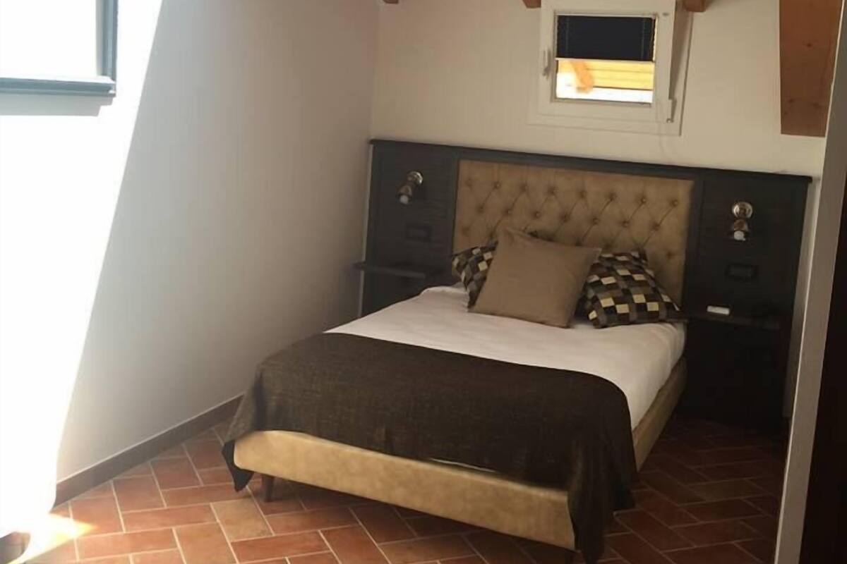 A bedroom with a sloped ceiling, a bed with a tufted headboard, a window, and a small skylight.