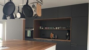 Moderni keittiö, jossa on tummat kaapit, puinen työtaso ja seinälle ripustetut kattilat.
