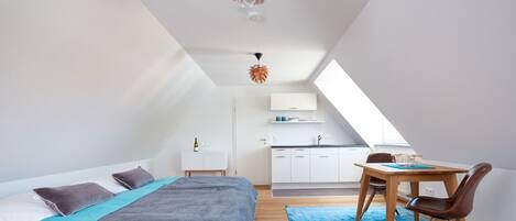 Et moderne loftværelse med en stor seng, spiseplads og et køkken.