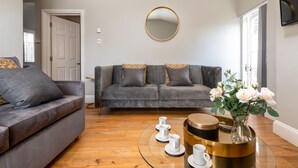 Una sala de estar moderna con un sofá gris, una mesa de centro con adornos y un espejo grande en la pared.