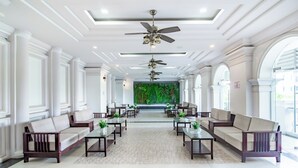 Um hall amplo com teto alto, diversas áreas de estar e vista para uma parede verde ao fundo.