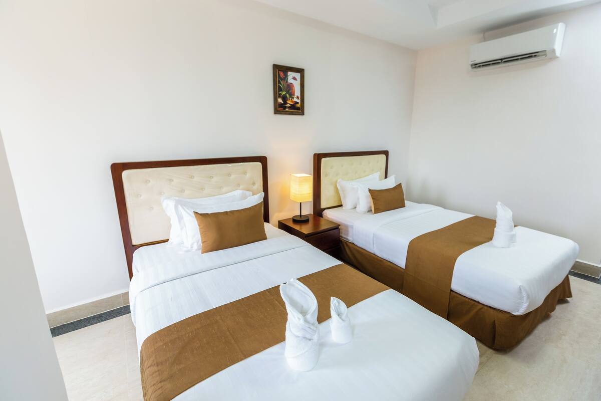 A hotel room with two beds, each with a headboard, a nightstand, a lamp, and a framed picture on the wall.