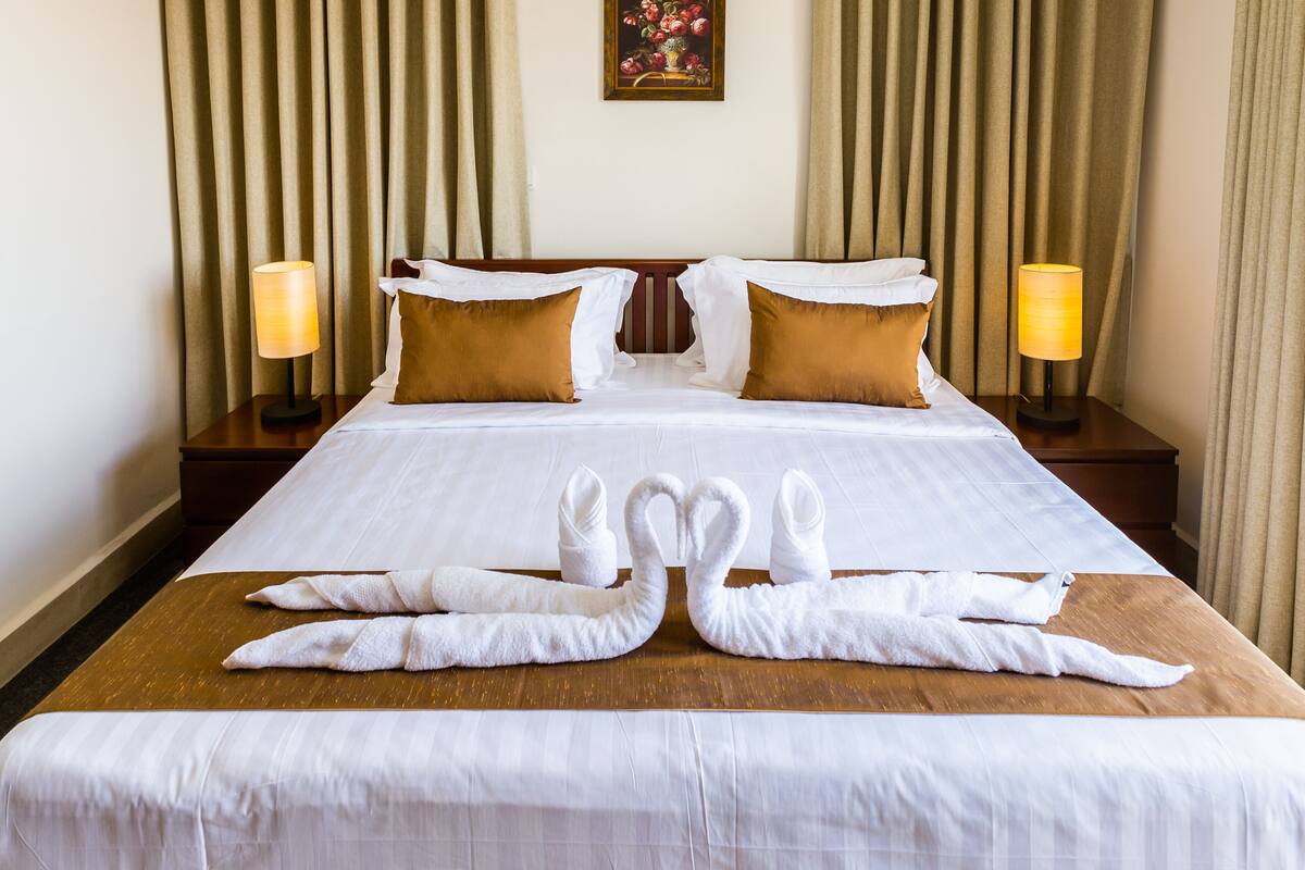 A neatly made bed with white linens and two brown pillows, flanked by two bedside lamps.
