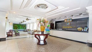 Um hall espaçoso com balcão de recepção, um vaso grande com flores e um mural verde na parede.