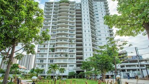 Um edifício residencial com vários andares, varandas, rodeado por vegetação e um caminho pavimentado.