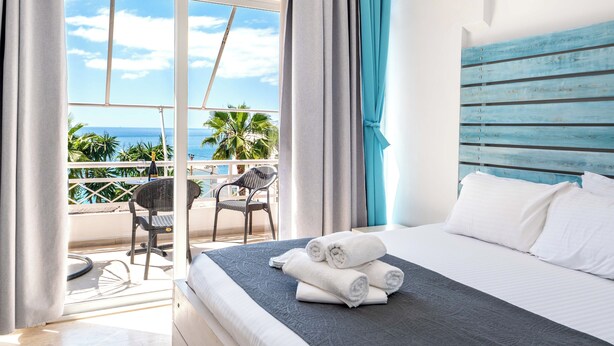 Una habitació d'hotel amb llit, un balcó amb una cadira i vista a l'oceà.