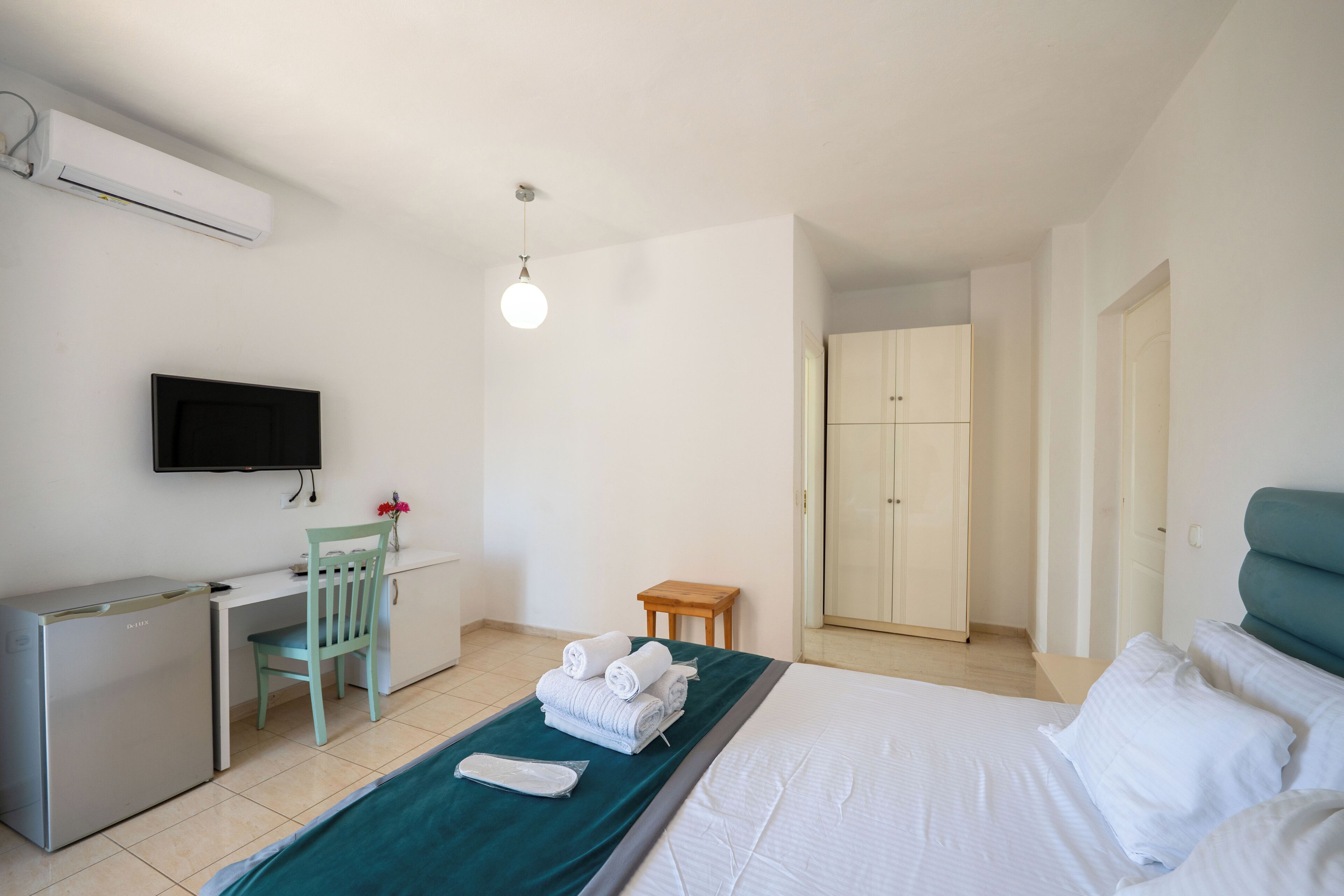 Habitación de hotel con cama, escritorio, silla, televisor, armario y puerta del baño.