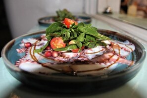 A bowl of food with spinach, cherry tomatoes, and octopus on a plate. - Hotel Saranda (Sarandë)