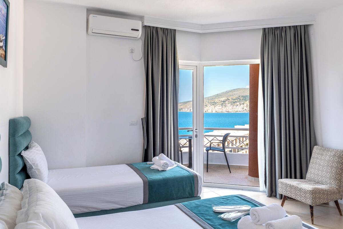 Habitación de hotel con dos camas, un balcón y vistas al mar, además de una silla.