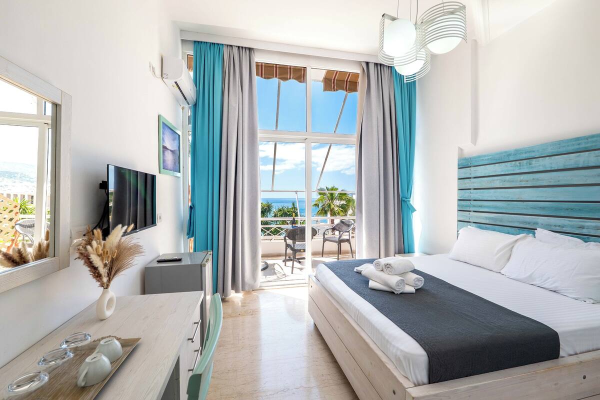 Habitación de hotel con cama, escritorio, televisión, ventana con cortinas y vista al océano.