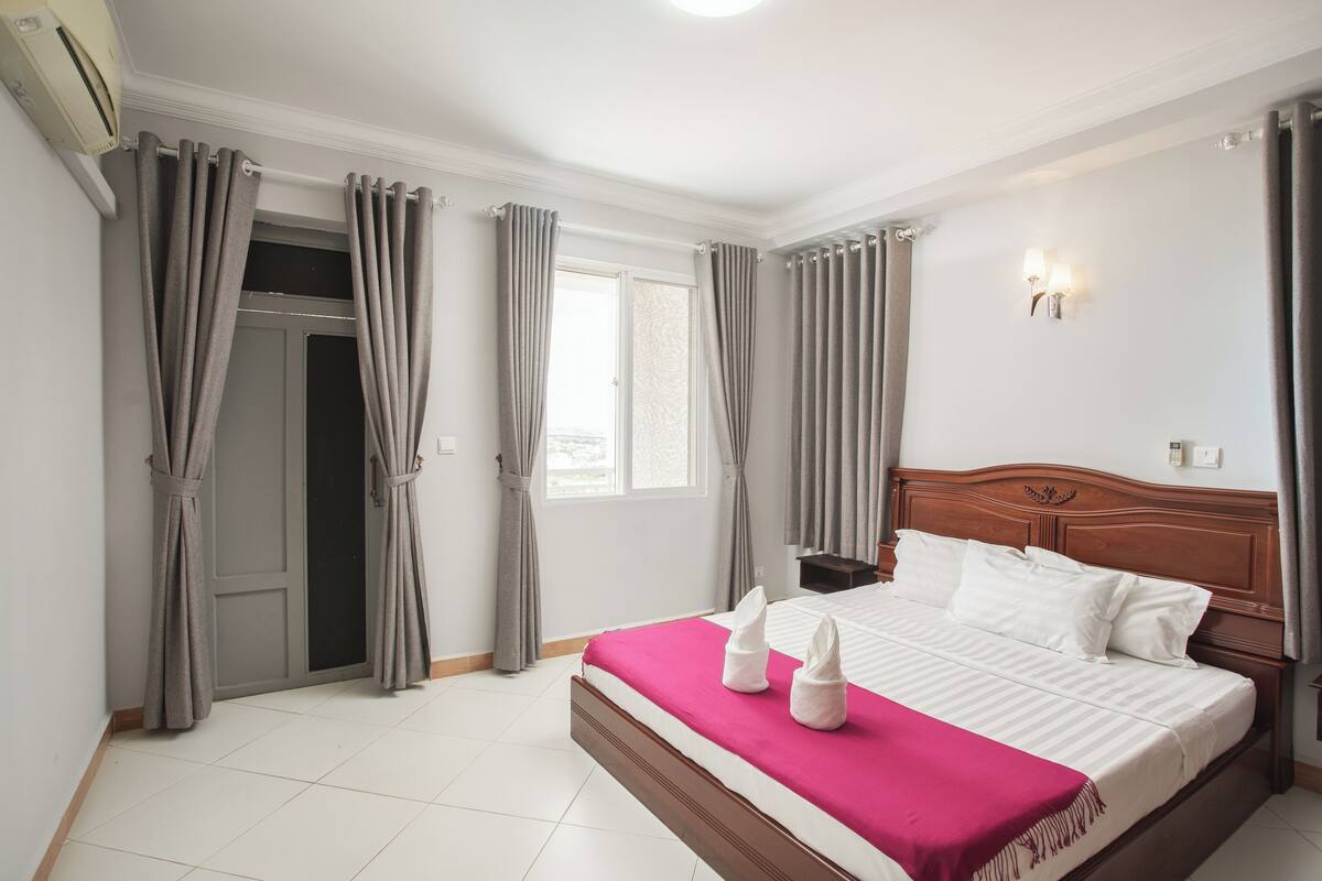 A hotel room with a bed, curtains, a window, and a wall-mounted light fixture.