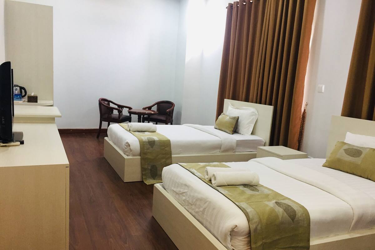 A hotel room with two single beds, a desk with a chair, and a television.