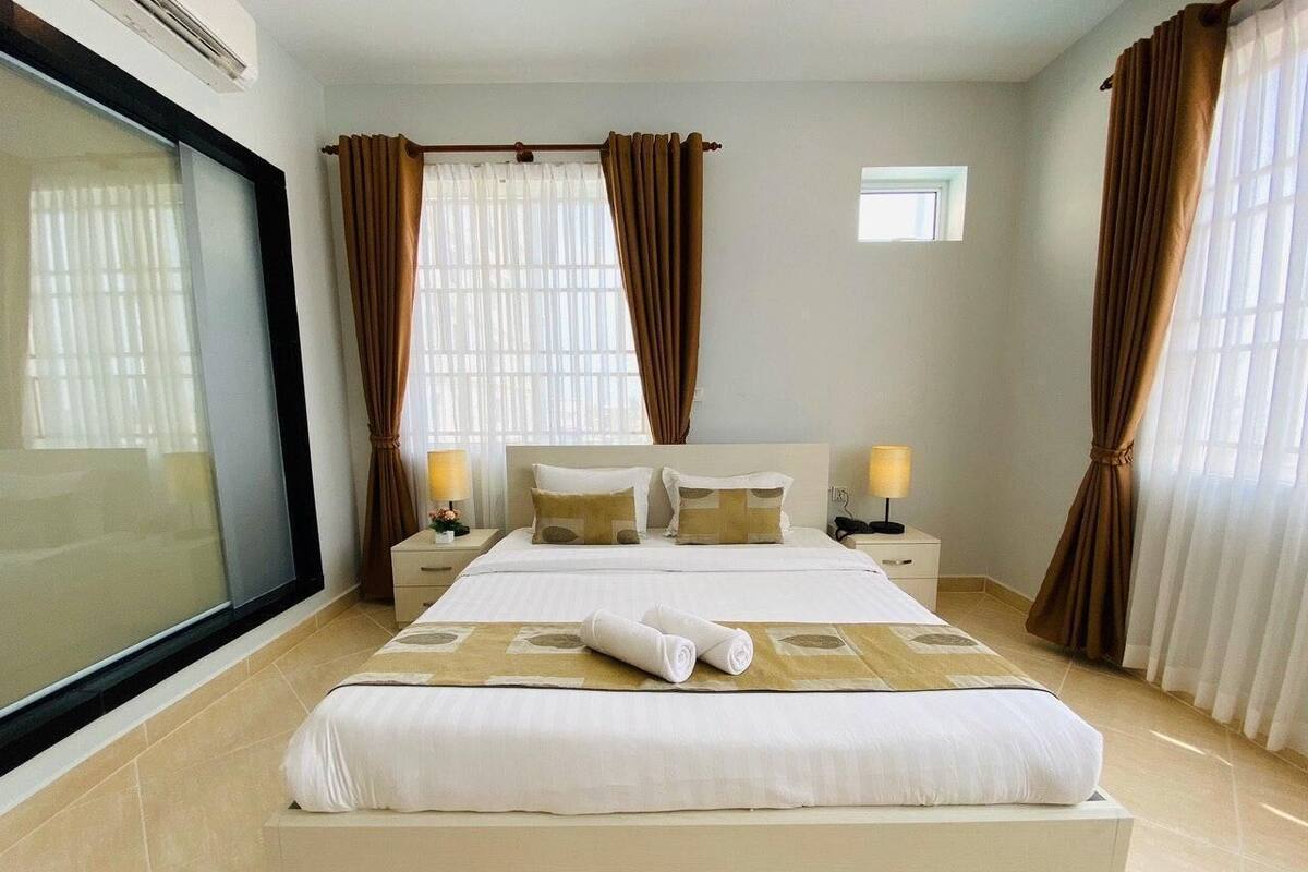 A hotel room with a large bed, two bedside tables, a window, and curtains.