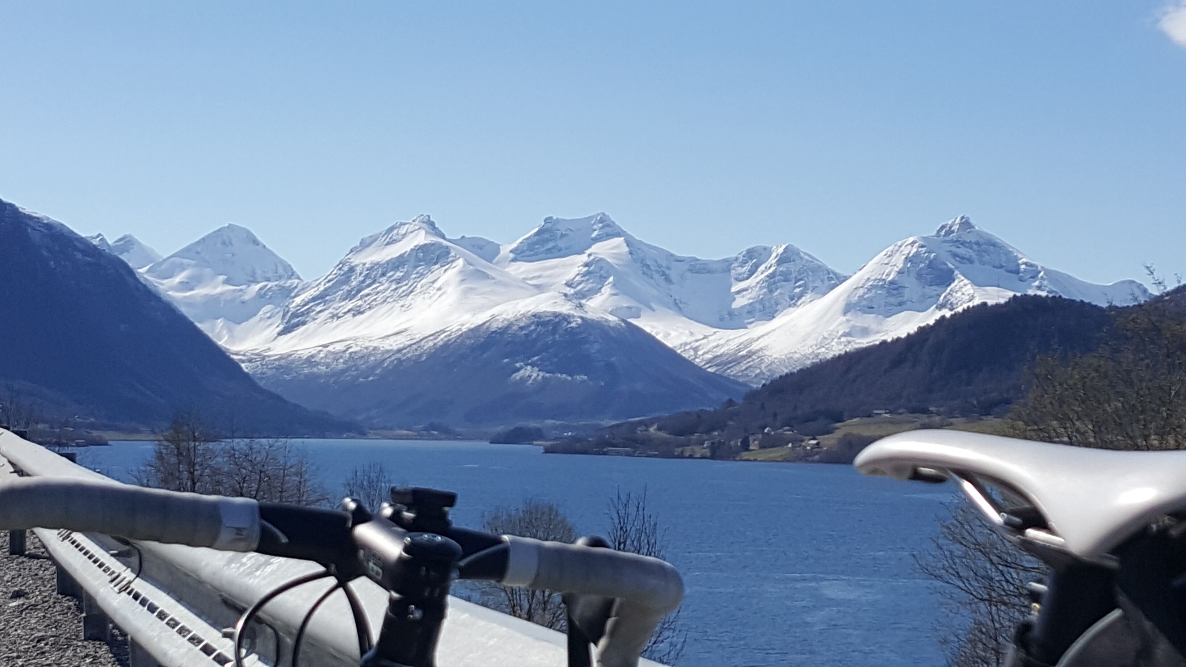 Una bicicleta estacionada a orillas de un lago, con montañas nevadas al fondo.