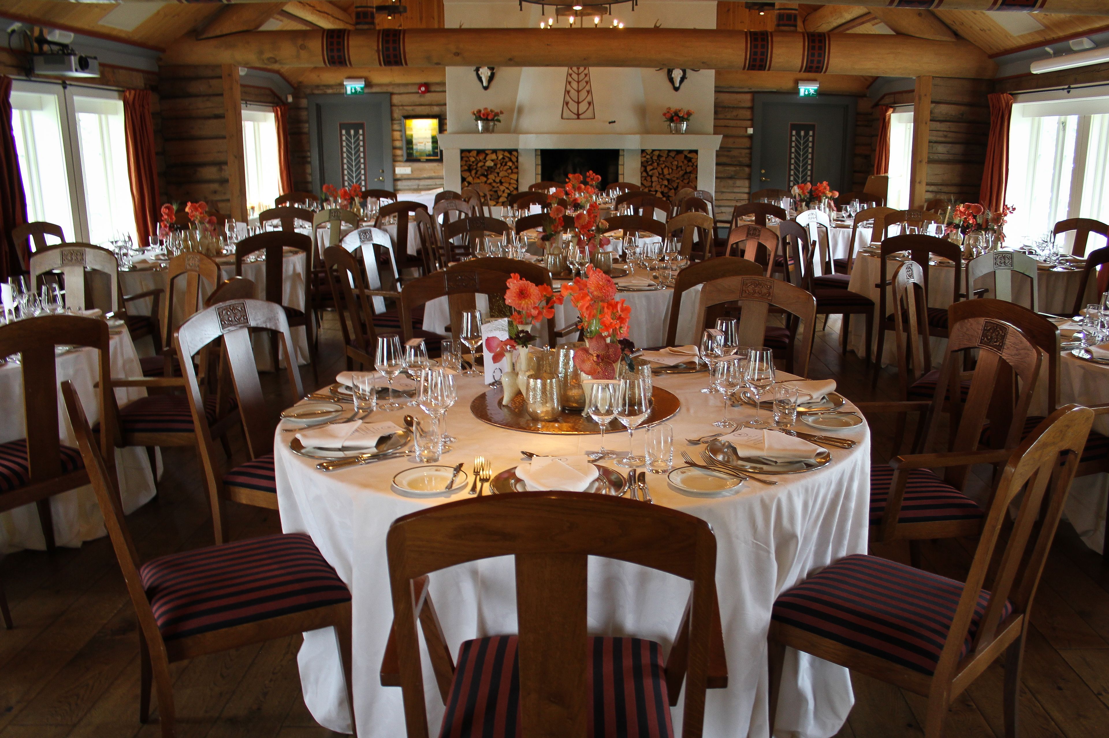 A dining area with round tables set for multiple guests, wooden chairs, and floral centerpieces.