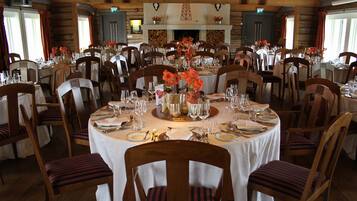 A dining area with round tables set for multiple guests, wooden chairs, and floral centerpieces.