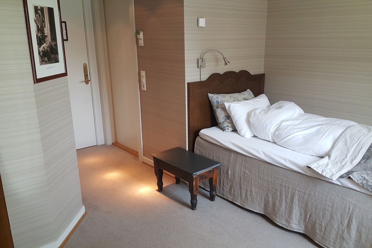 A bedroom with a bed, bedside table, and a door leading to another room.