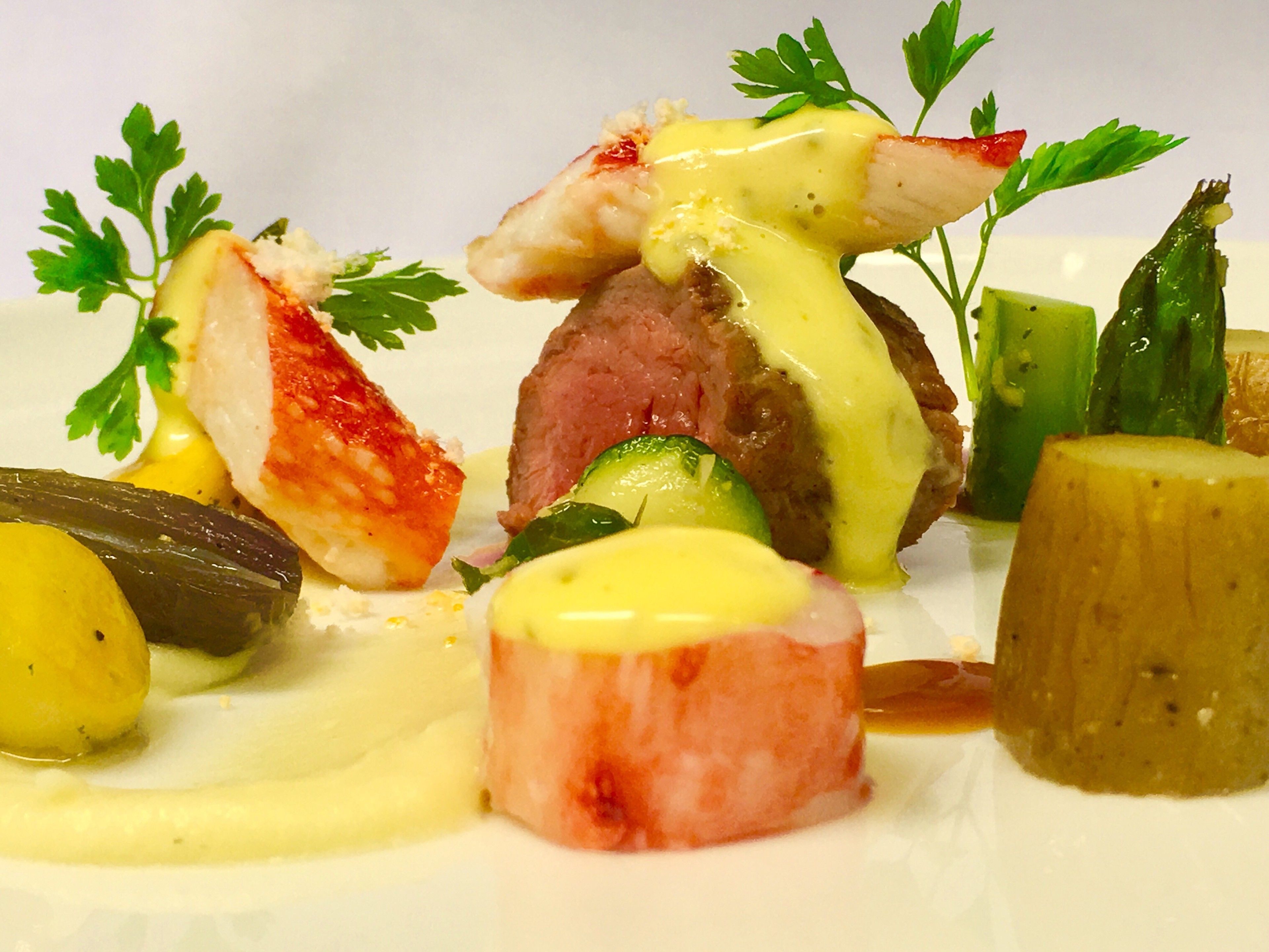 A plated dish with various food items including a piece of meat, a fish, and vegetables, garnished with parsley.