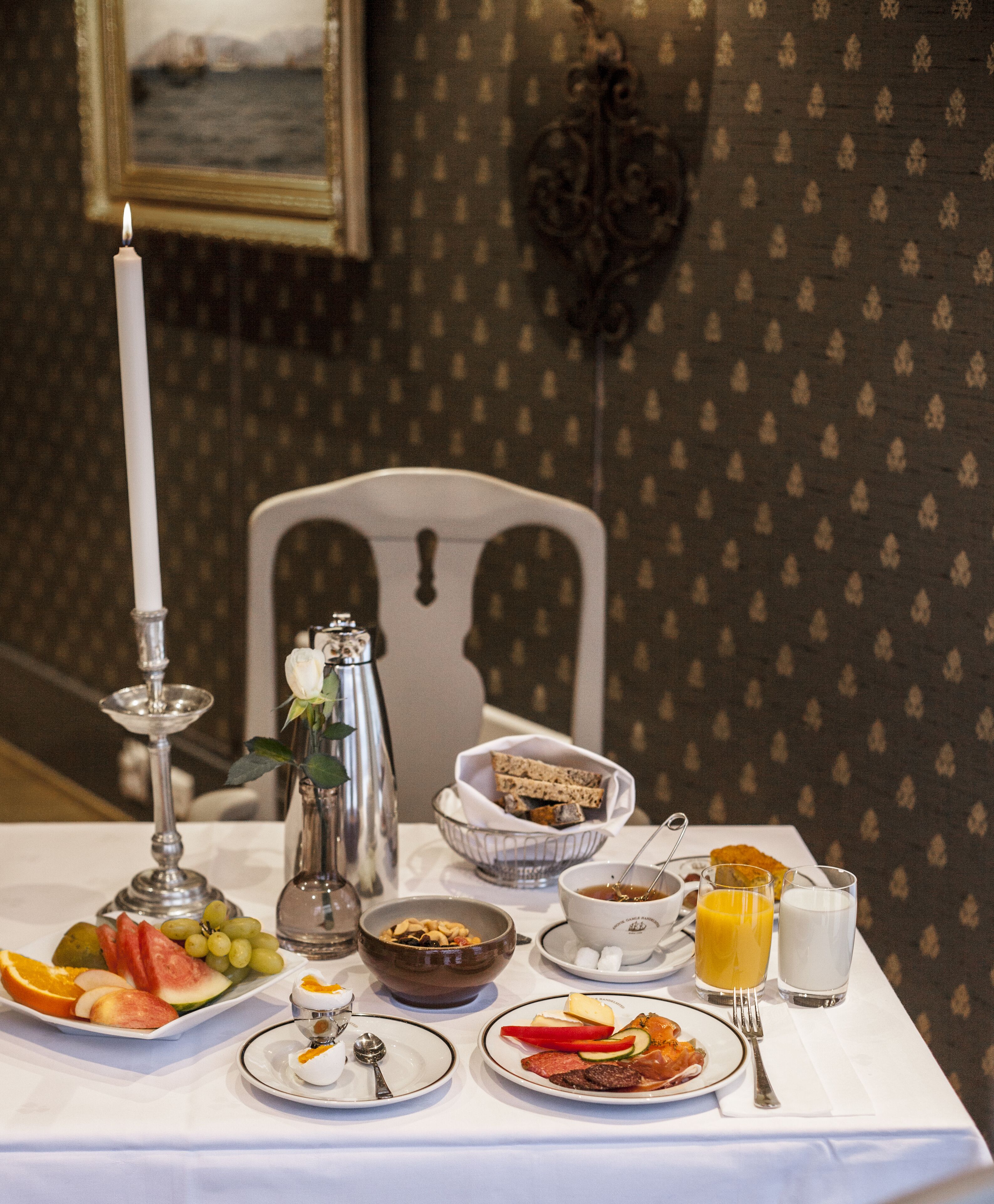 Ett frukostbord med ett varierat utbud av matvaror, inklusive frukt, bröd och drycker, uppdukat på en vit duk.