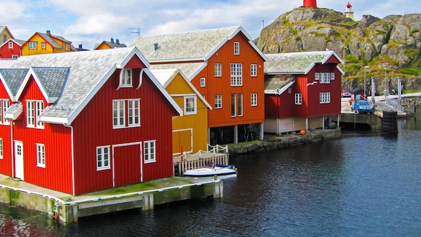 A waterfront with red and yellow buildings, a lighthouse, and a dock with a small boat.