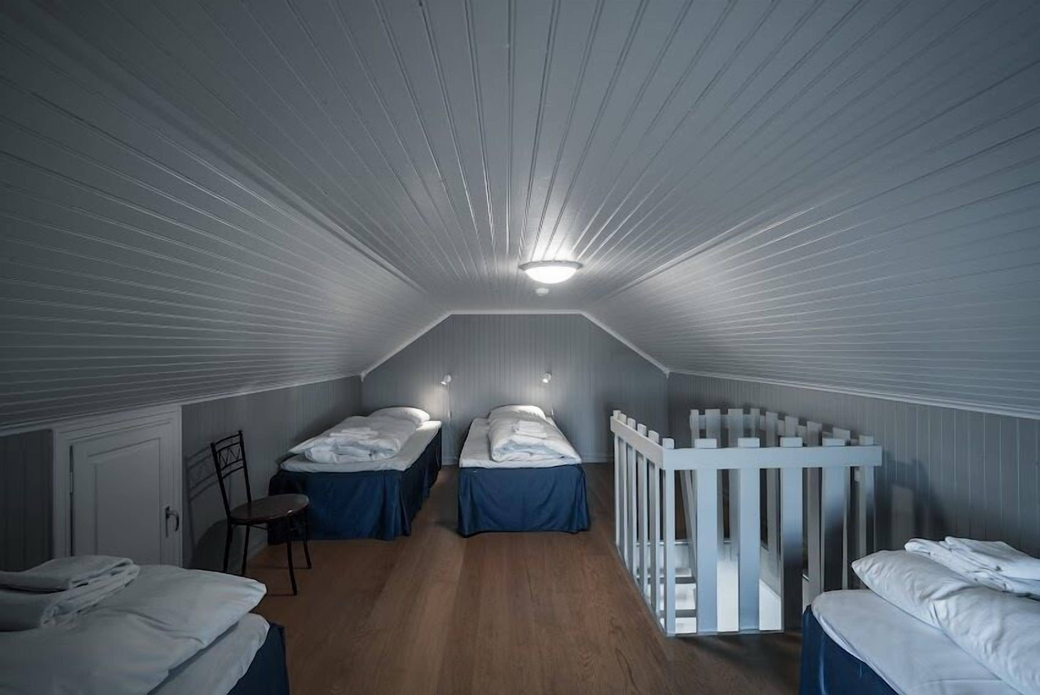 A dormitory room with two beds, a white crib, and a wooden floor.