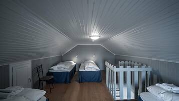 A dormitory room with two beds, a white crib, and a wooden floor.