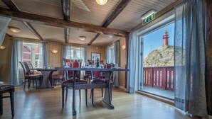 A dining area with a wooden table and chairs, large windows with a view of a lighthouse, and a wooden ceiling.