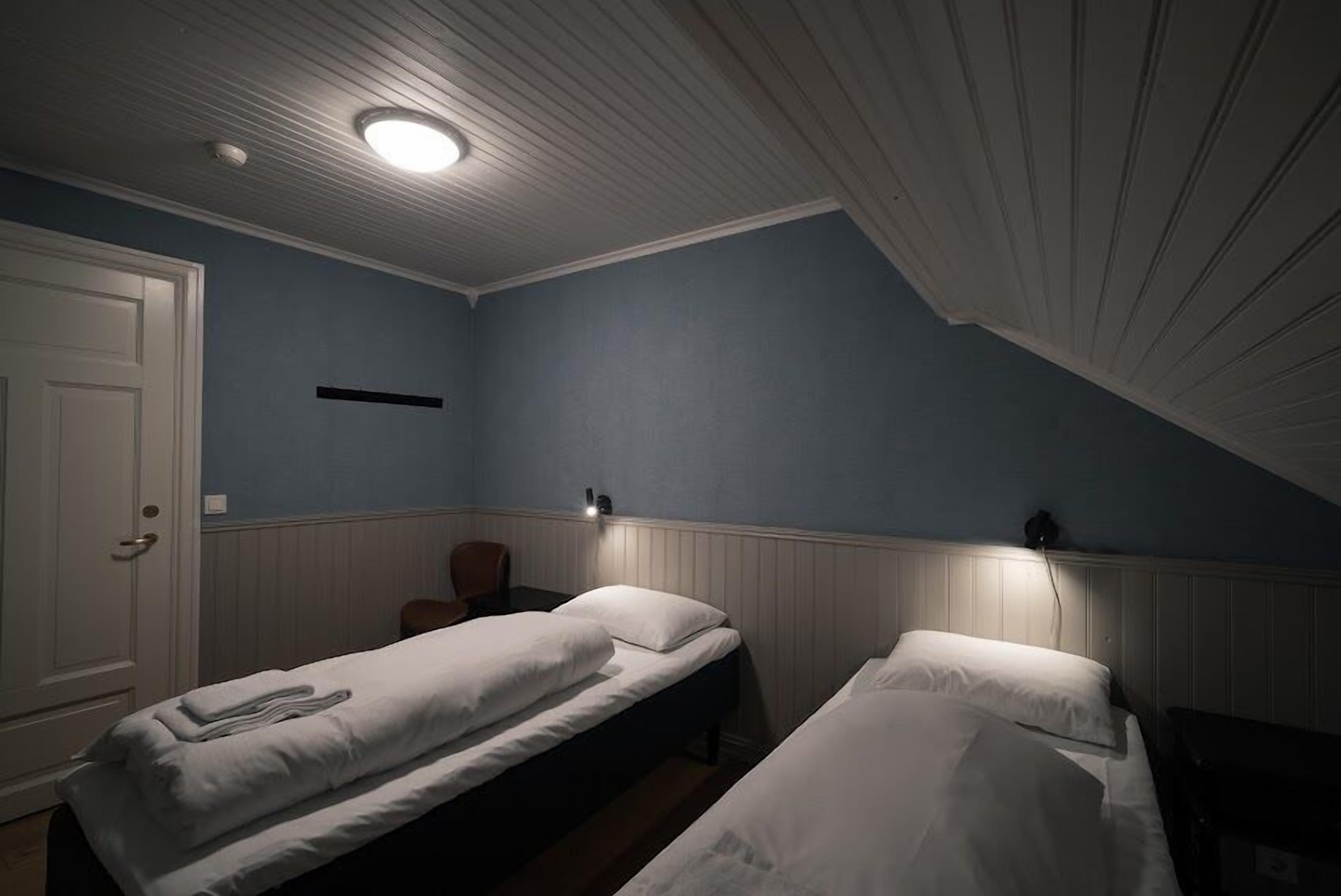 A room with two single beds, a door, a light fixture, and a wall-mounted shelf.