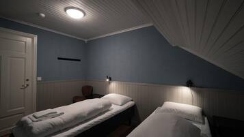 A room with two single beds, a door, a light fixture, and a wall-mounted shelf.