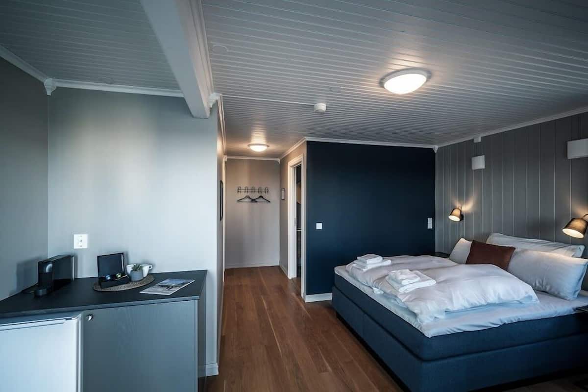A modern hotel room with a bed, bedside table, and a desk with a computer and a coffee machine.