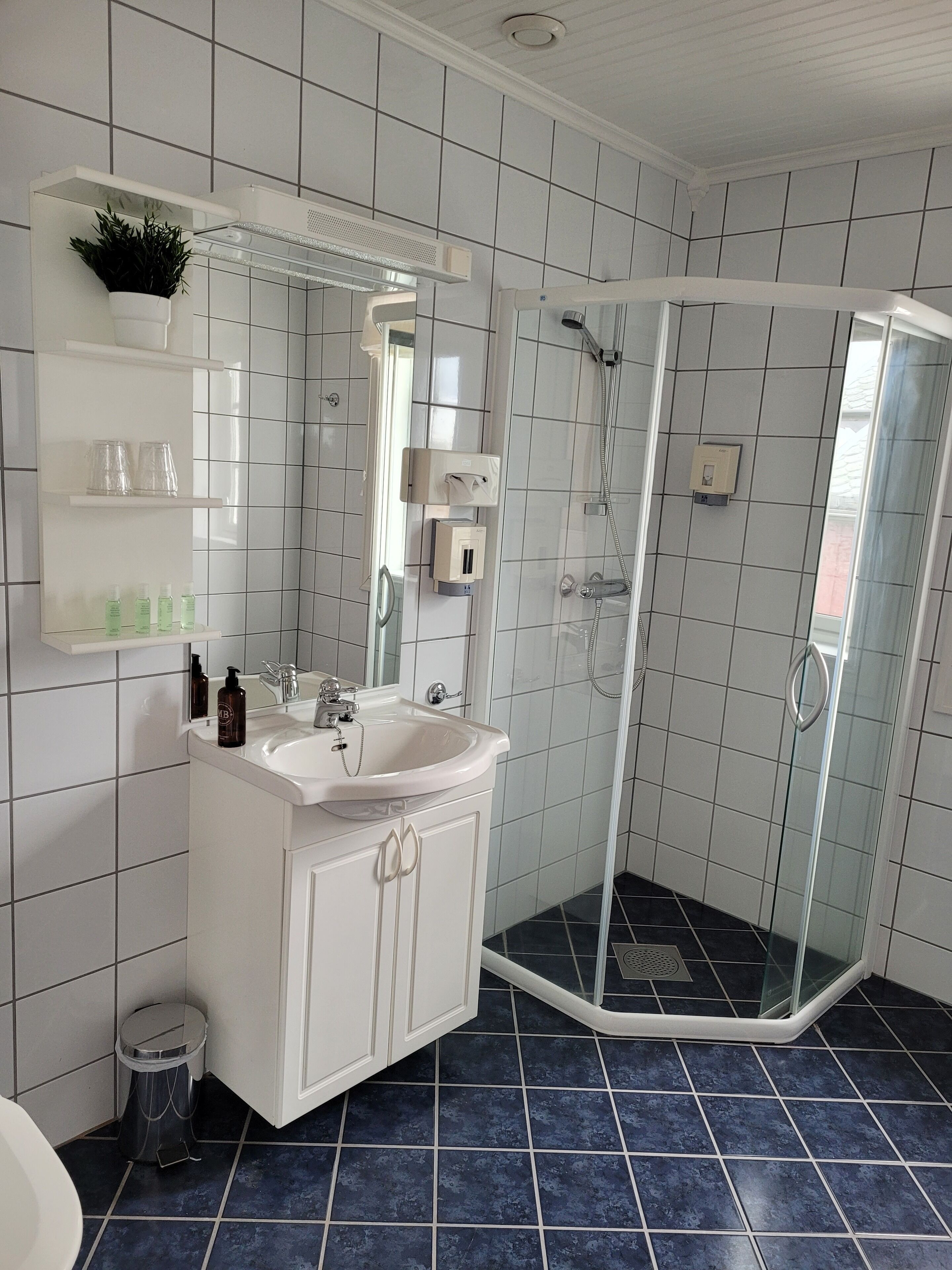 A modern bathroom with a glass-enclosed shower, white tiled walls, a white sink, and a mirror.